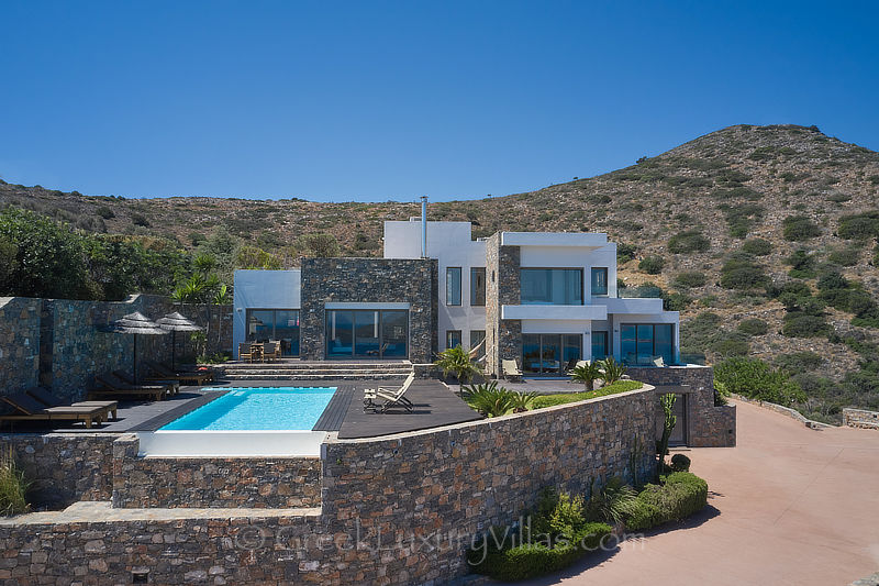 aerial drone view of modern luxury villa with heated pool overlooking elounda bay